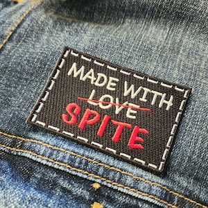 May include: Black patch with white stitching and the text "Made with Love" crossed out and "SPITE" written in red.