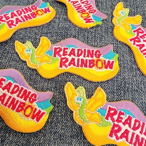 May include: A set of six colorful iron-on patches featuring a cartoon worm and the text "Reading Rainbow".