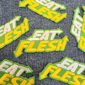 Może przedstawiać: Pięć haftowanych naszywek w kolorze zielonym i żółtym z napisem "Eat Flesh" w kolorze białym. Naszywki znajdują się na niebieskim tle z dżinsu.