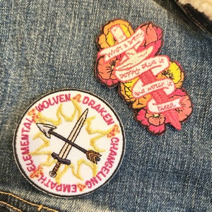 May include: Two embroidered patches. One is round and white with a yellow sun, two crossed swords, and the text "WOLVEN DRAKEN CHANSELING EMPATHS ELEMENTAL". The other is a pink and orange floral patch with a red sword and the text "what a pretty poppy place it and watch it bleed".