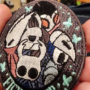May include: Embroidered patch with a black background featuring two white characters with black eyes and mouths. The characters are surrounded by blue, pink, and teal accents. The patch has a teal border with the text "The Night We Met" in a white font.