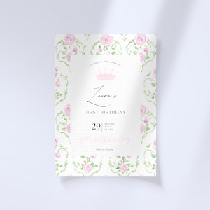 May include: A white invitation with a pink floral pattern and a crown. The text reads "Please join us to celebrate Laura's First Birthday, Saturday July 29 at 3 pm. RSVP to Claudia."