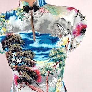 May include: A white dress with a mandarin collar and short sleeves. The dress features a colourful print of a Japanese landscape with mountains, trees, and water.