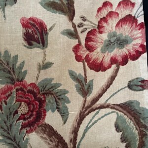 May include: A beige fabric with a floral pattern. The flowers are red, pink, and white with green leaves. The fabric has a vintage look.