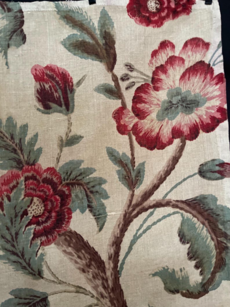 May include: A beige fabric with a floral pattern. The flowers are red, pink, and white with green leaves. The fabric has a vintage look.