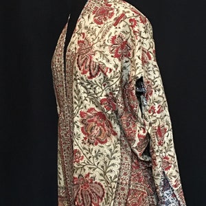 Pu&ograve; includere: Un kimono color crema con stampa floreale rossa e verde. Il kimono ha una silhouette lunga e fluida e un collo largo e aperto.