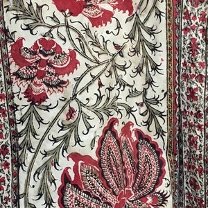 Pu&ograve; includere: Un tessuto bianco con un motivo floreale rosso e nero. I fiori sono stilizzati e hanno un design di tipo paisley. Il tessuto ha un aspetto e una sensazione vintage.