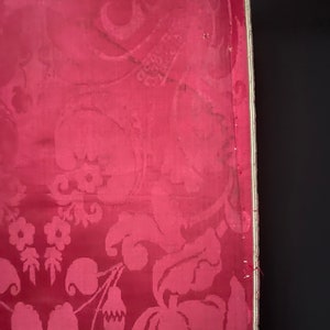 May include: A close-up of a red fabric with a white floral pattern. The fabric has a textured surface and a white border.