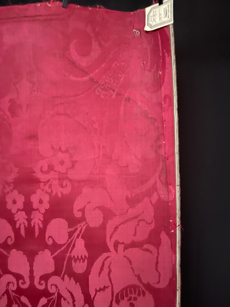 May include: A close-up of a red fabric with a white floral pattern. The fabric has a textured surface and a white border.