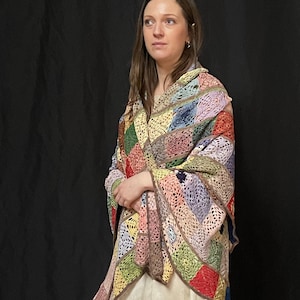 May include: A woman wearing a multi-colored crochet shawl with a granny square pattern. The shawl is made of different shades of pink, green, blue, yellow, and red yarn.