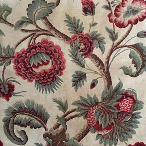 May include: A beige fabric with a repeating pattern of red and green floral designs. The flowers are stylized and have a vintage look.