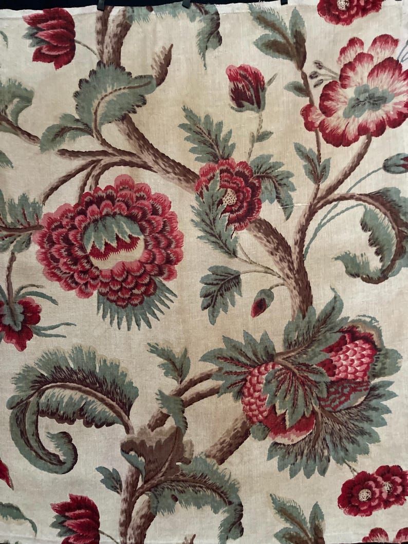 May include: A beige fabric with a repeating pattern of red and green floral designs. The flowers are stylized and have a vintage look.