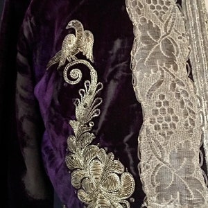 May include: A purple velvet jacket with silver embroidery of a bird and floral design. The jacket has a silver lace trim.