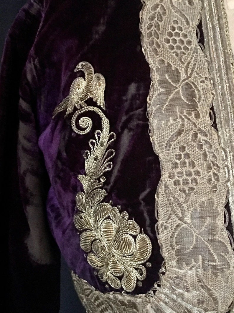 May include: A purple velvet jacket with silver embroidery of a bird and floral design. The jacket has a silver lace trim.