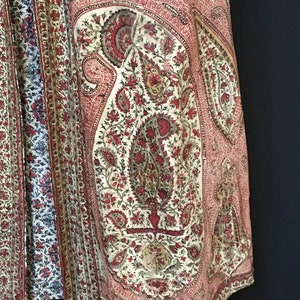 Pu&ograve; includere: Primo piano di un tessuto con motivo paisley rosso e bianco. Il tessuto presenta un disegno floreale con un grande motivo paisley al centro.