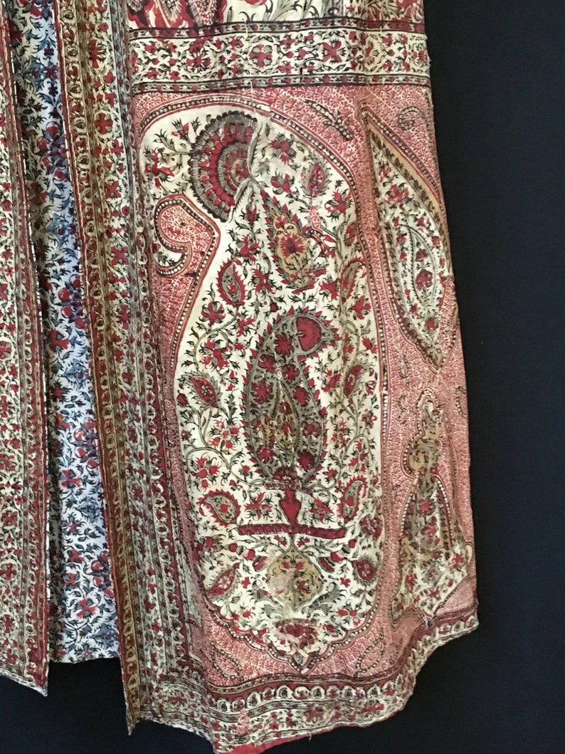 Pu&ograve; includere: Primo piano di un tessuto con motivo paisley rosso e bianco. Il tessuto presenta un disegno floreale con un grande motivo paisley al centro.