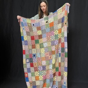 May include: A large, colorful crocheted blanket with a patchwork design. The blanket is made up of squares in various colors, including red, orange, yellow, green, blue, purple, and brown. The squares are joined together with a white crocheted border.