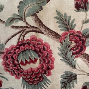 May include: A close-up of a fabric with a floral pattern. The fabric features a large pink flower with green leaves and a brown branch. The background is a light beige color.