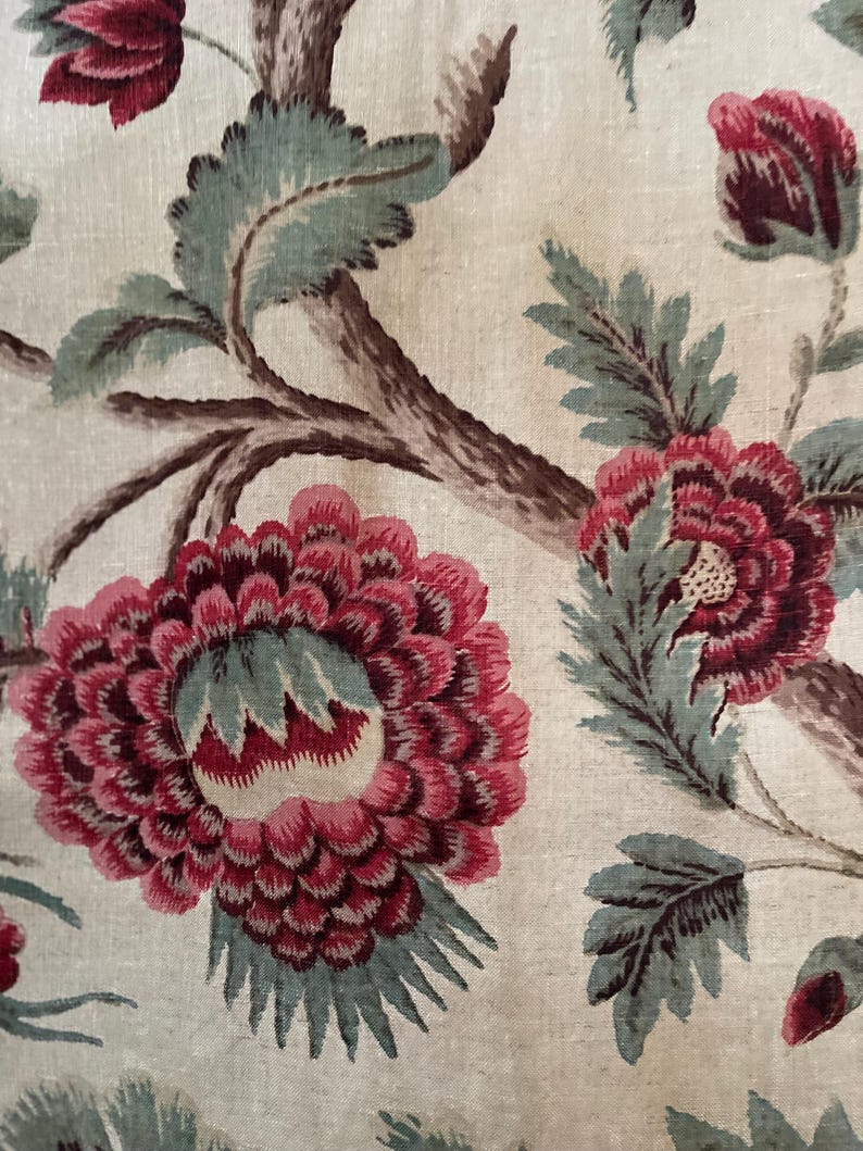 May include: A close-up of a fabric with a floral pattern. The fabric features a large pink flower with green leaves and a brown branch. The background is a light beige color.