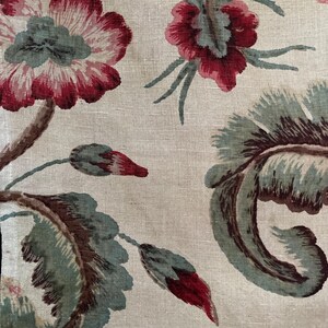 May include: A beige fabric with a floral pattern. The flowers are red, pink, and green. The fabric has a linen texture.