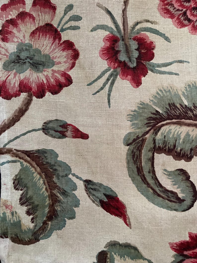 May include: A beige fabric with a floral pattern. The flowers are red, pink, and green. The fabric has a linen texture.