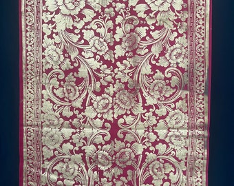 May include: A red fabric with a gold floral pattern. The fabric has a border with a repeating geometric design.