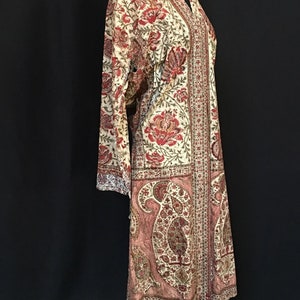 Pu&ograve; includere: Una lunga veste color crema con stampa paisley in tonalit&agrave; di rosso, rosa e verde. La veste ha un collo a V e maniche lunghe.