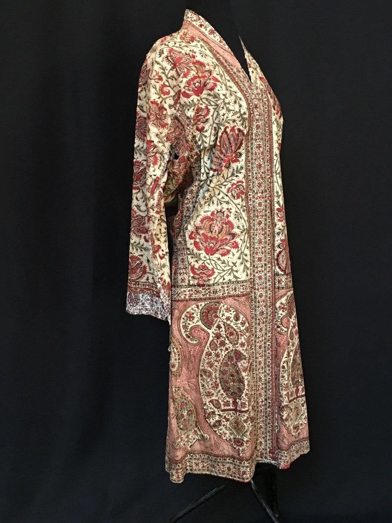 Pu&ograve; includere: Una lunga veste color crema con stampa paisley in tonalit&agrave; di rosso, rosa e verde. La veste ha un collo a V e maniche lunghe.