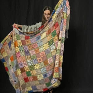 May include: A colorful crocheted blanket with a patchwork design in shades of pink, blue, green, yellow, and red. The blanket is made of squares with a delicate lace pattern.
