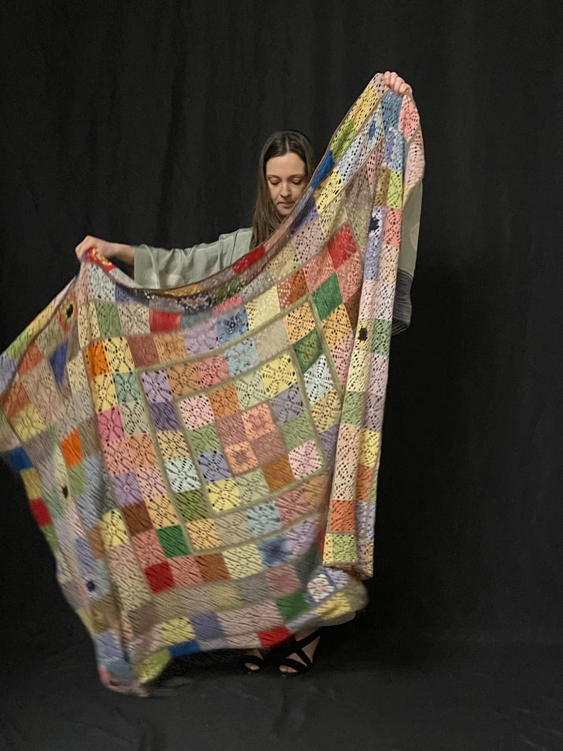 May include: A colorful crocheted blanket with a patchwork design in shades of pink, blue, green, yellow, and red. The blanket is made of squares with a delicate lace pattern.