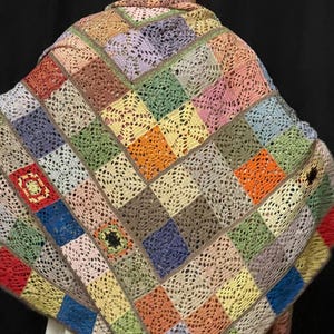 May include: A colorful crocheted shawl with a patchwork design featuring squares in various shades of pink, blue, green, orange, and brown.