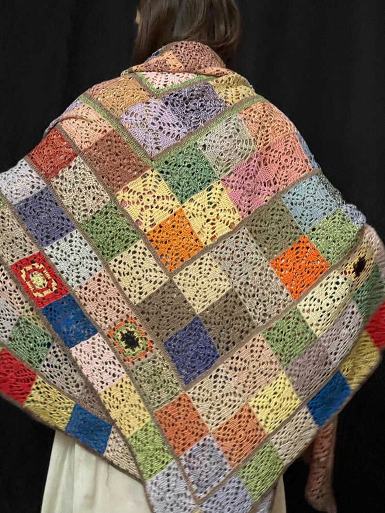 May include: A colorful crocheted shawl with a patchwork design featuring squares in various shades of pink, blue, green, orange, and brown.