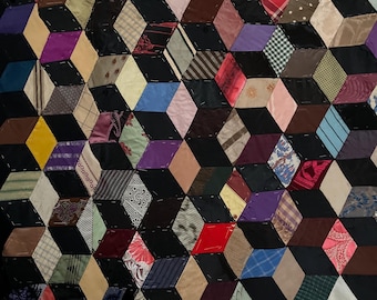 May include: A handmade quilt with a geometric design. The quilt features a repeating pattern of diamond shapes in various colors, including red, blue, purple, and brown, set against a black background. The quilt is made of fabric scraps.