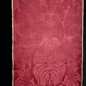 May include: A close-up of a red damask fabric with a floral pattern. The fabric has a subtle sheen and a delicate texture.