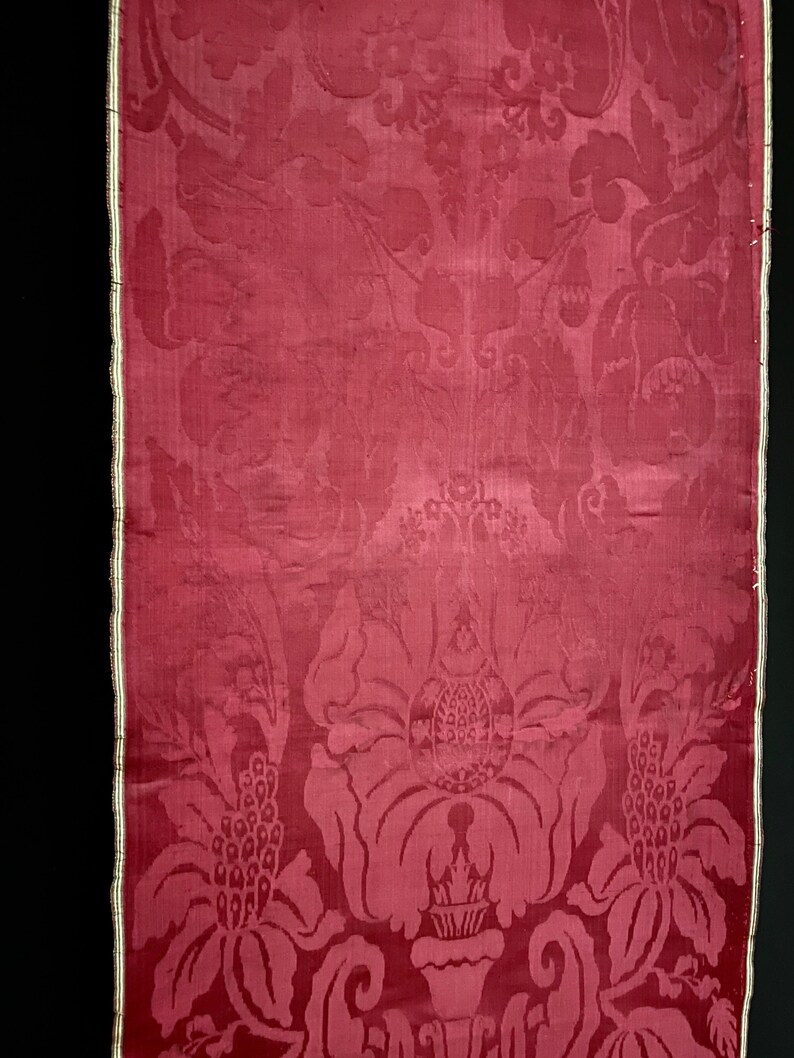 May include: A close-up of a red damask fabric with a floral pattern. The fabric has a subtle sheen and a delicate texture.