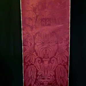 May include: A close-up of a deep red fabric with a damask pattern. The fabric has a subtle sheen and a delicate floral design.