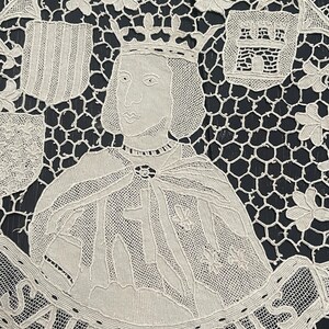 May include: Cream-colored lace doily featuring a portrait of a crowned figure, possibly a historical personage. The design includes heraldic shields, floral accents, and the text "SAINT LOUIS" in a banner. The intricate lace work is set against a dark background.