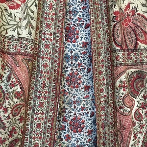 Pu&ograve; includere: Primo piano di un tessuto con un motivo floreale rosso, bianco e blu che si ripete. Il tessuto ha un motivo paisley negli angoli.