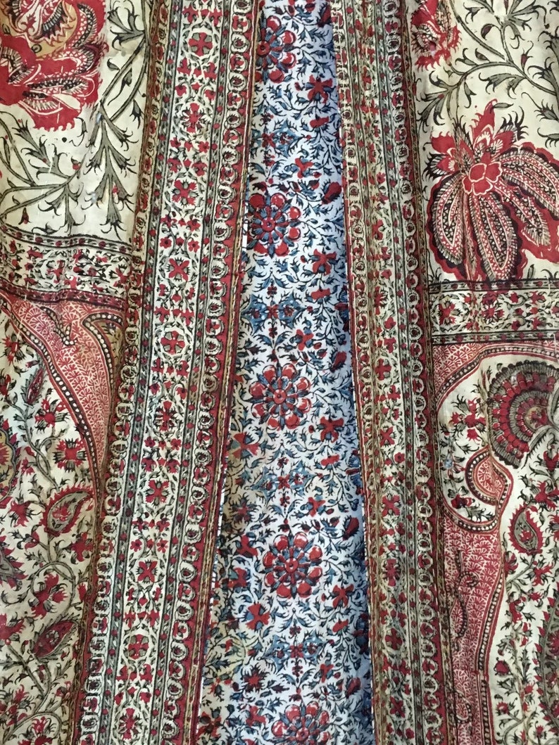 Pu&ograve; includere: Primo piano di un tessuto con un motivo floreale rosso, bianco e blu che si ripete. Il tessuto ha un motivo paisley negli angoli.