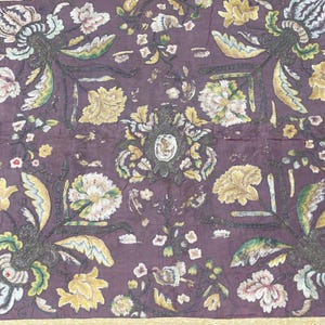 May include: Close-up of a textile featuring a repeating floral design. The fabric is a deep purple with embroidered flowers in cream, yellow, and green. The edges are trimmed with a gold border, giving a vintage appearance.