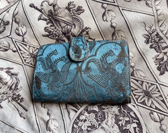 May include: A blue and black patterned wallet with a decorative clasp. The wallet is made of a soft, textured fabric.