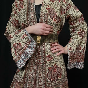 Pu&ograve; includere: Una lunga veste color crema con stampa floreale in tonalit&agrave; di rosso, marrone e blu. La veste ha una silhouette ampia e fluida e una cintura.