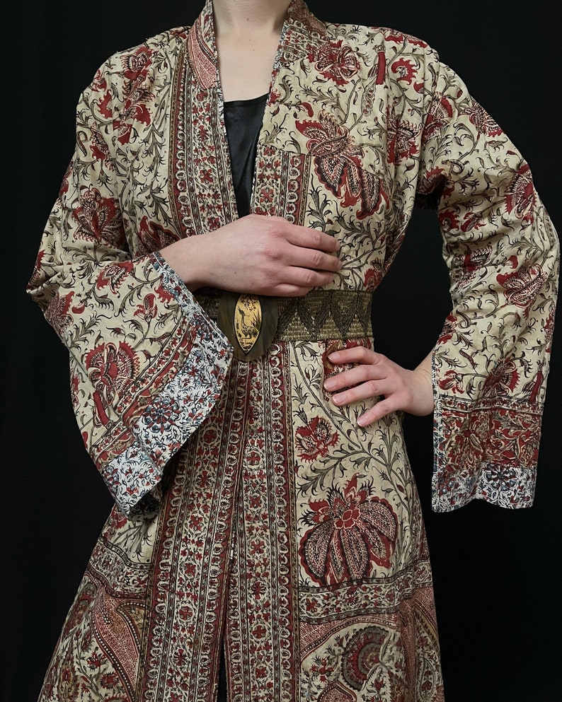 Pu&ograve; includere: Una lunga veste color crema con stampa floreale in tonalit&agrave; di rosso, marrone e blu. La veste ha una silhouette ampia e fluida e una cintura.