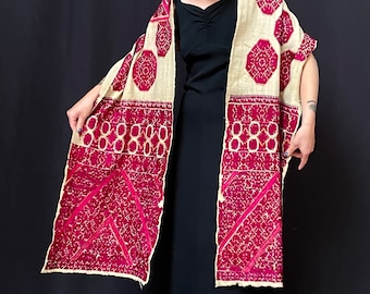 May include: A long, rectangular shawl with a cream background and intricate red embroidery. The shawl is folded in half and draped over the shoulders of a person wearing a black dress.