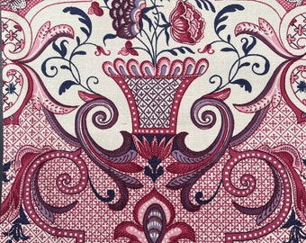 May include: Close-up of a decorative fabric with a floral design. The pattern features a central vase filled with flowers in shades of burgundy and pink, surrounded by swirling scrollwork and geometric shapes. The background is off-white.