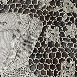 May include: Close-up of a beige lace doily with intricate floral and geometric patterns. The doily features a detailed design with flowers, leaves, and a delicate openwork mesh. The lace is finely crafted, showcasing the artistry of the textile.
