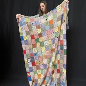 May include: A large, colorful crochet blanket with a patchwork design. The blanket is made up of squares of different colors, including pink, blue, green, yellow, and red. The blanket is crocheted in a delicate pattern, and the edges are finished with a simple border.