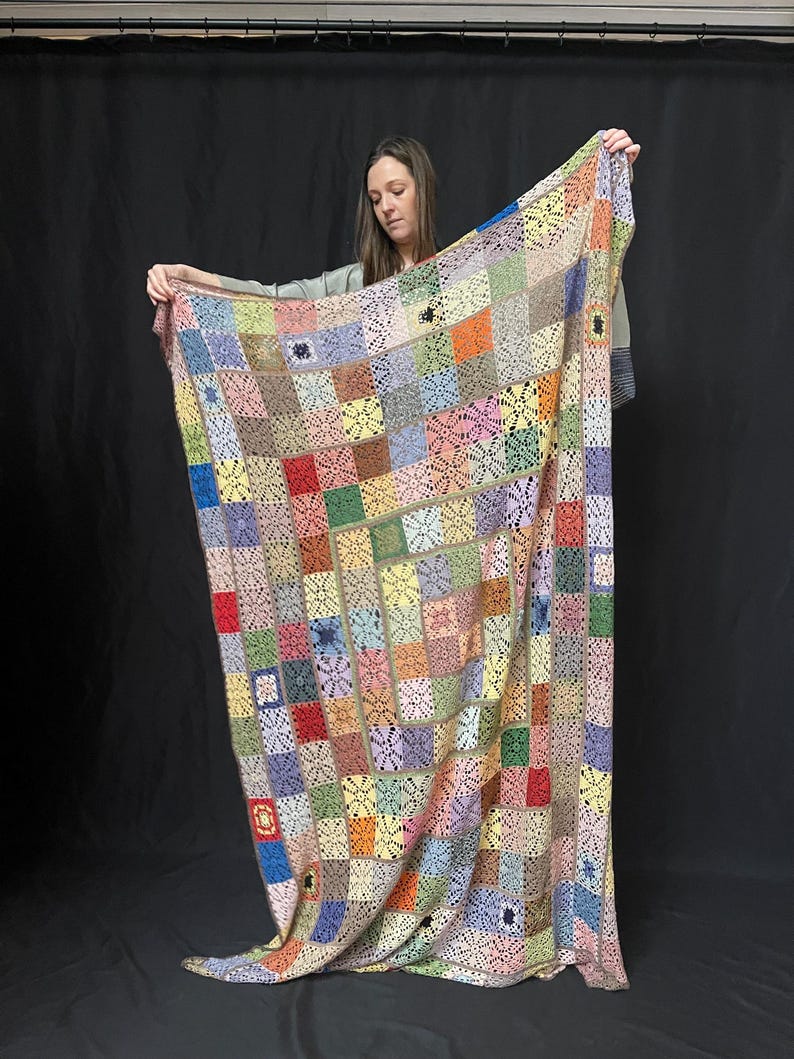 May include: A large, colorful crochet blanket with a patchwork design. The blanket is made up of squares of different colors, including pink, blue, green, yellow, and red. The blanket is crocheted in a delicate pattern, and the edges are finished with a simple border.