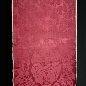 May include: A close-up of a red damask fabric with a floral pattern. The fabric has a white border and is woven with a raised design.