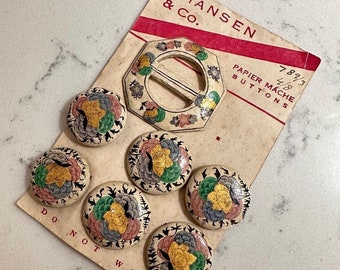 May include: A set of seven vintage paper mache buttons with floral designs in shades of pink, green, yellow, and blue. The buttons are on a card that reads "Johansen & Co. Papier Mache Buttons 7 8/3 4/8".